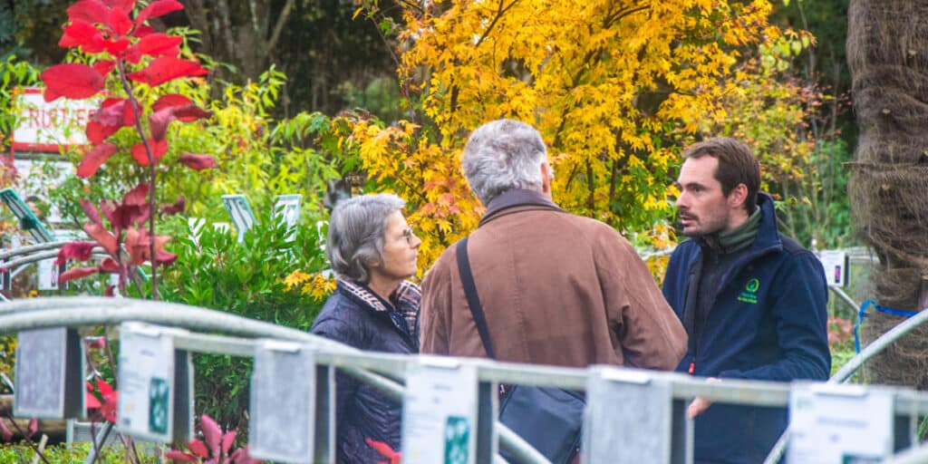 Trois personnes discutant dans un jardin automnal.