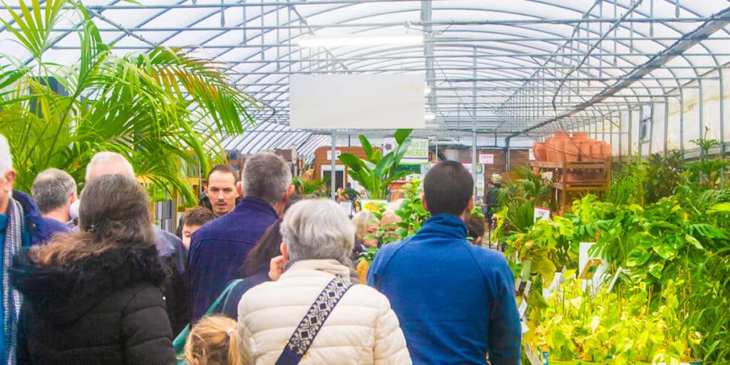 Foule dans jardinerie avec plantes vertes et serre.